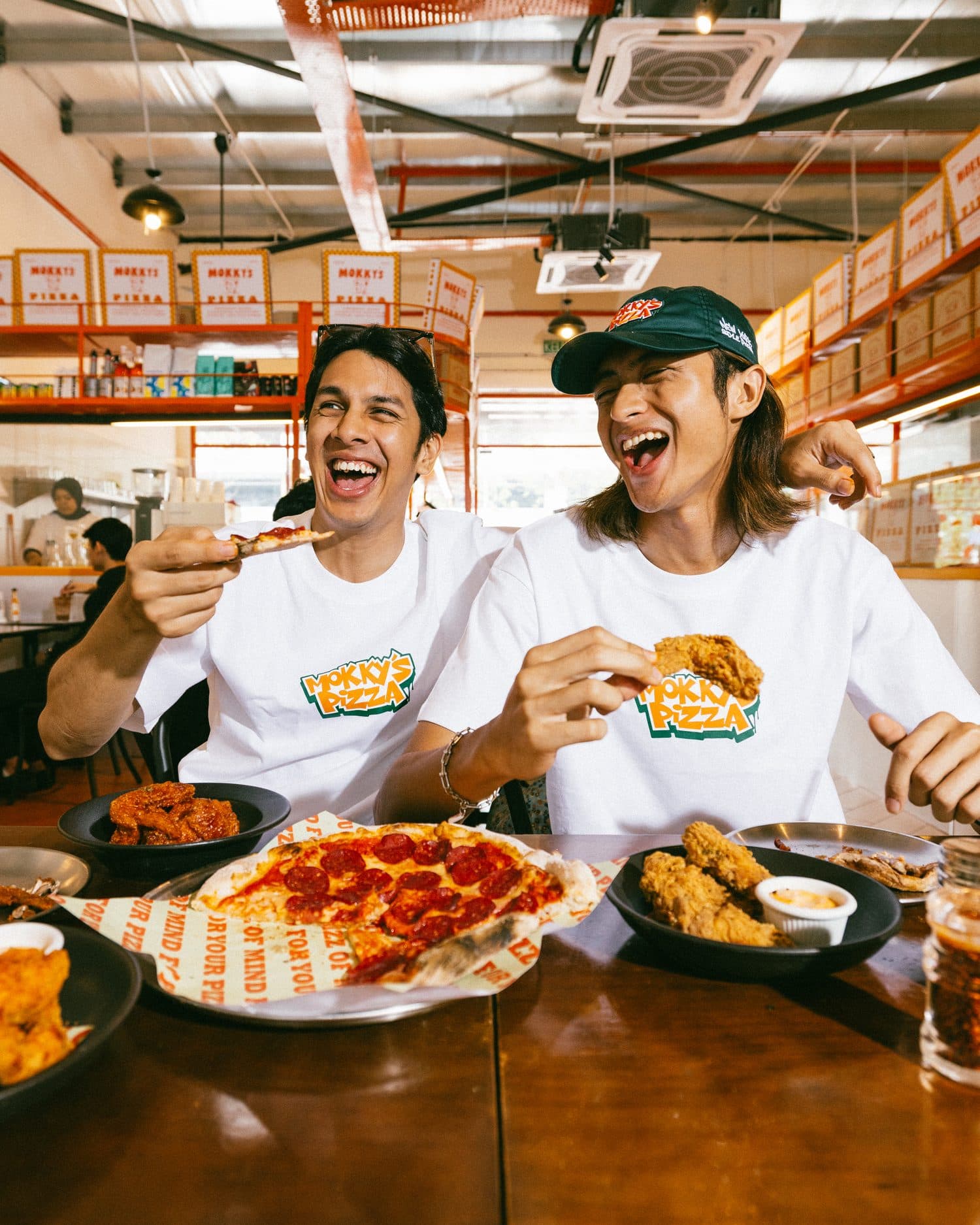 Two friends laughing over pepperoni pizza and fried chicken