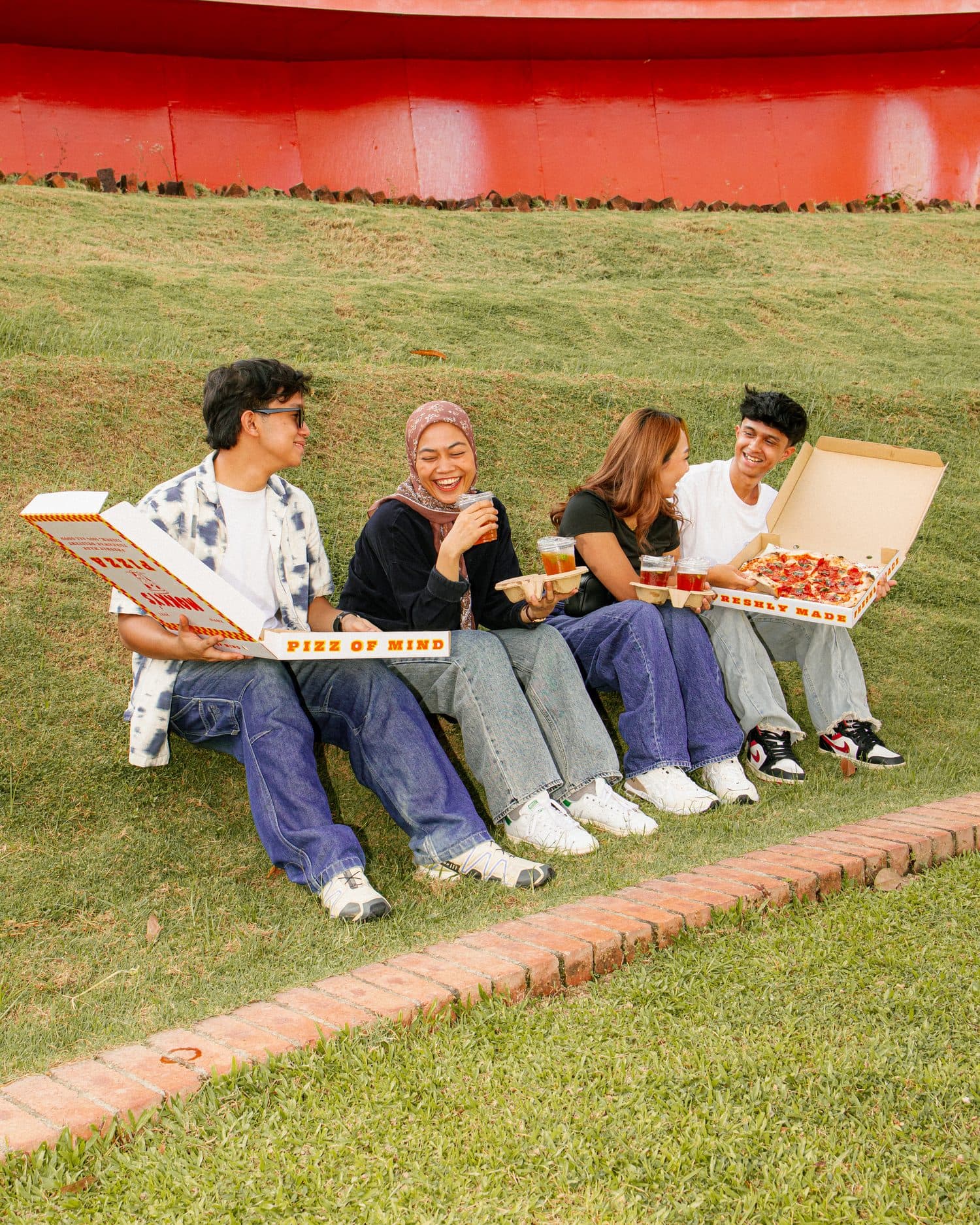 Four friends sharing Mokky's pizza on a grassy slope