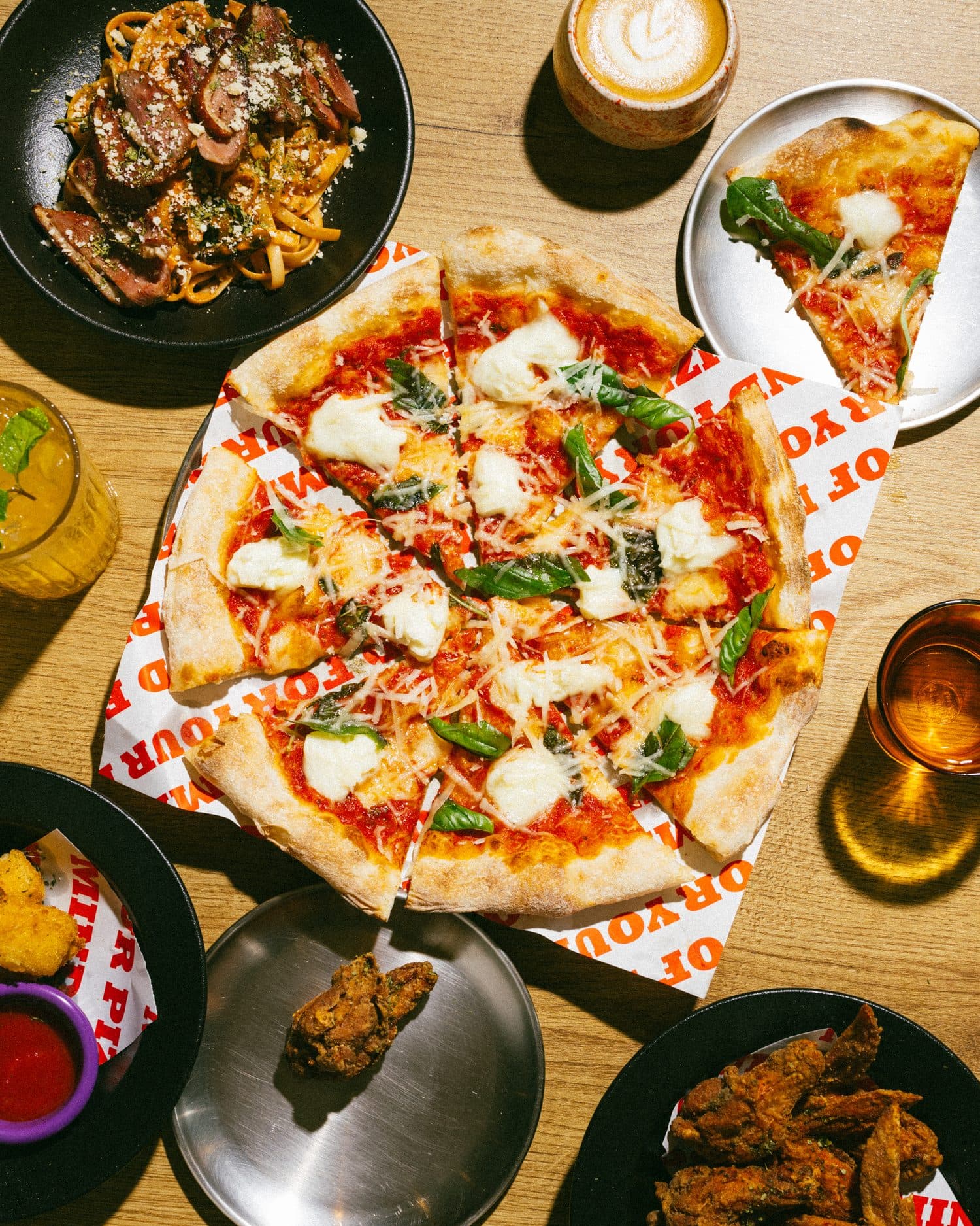 Pizzas, wings and drinks spread across a table